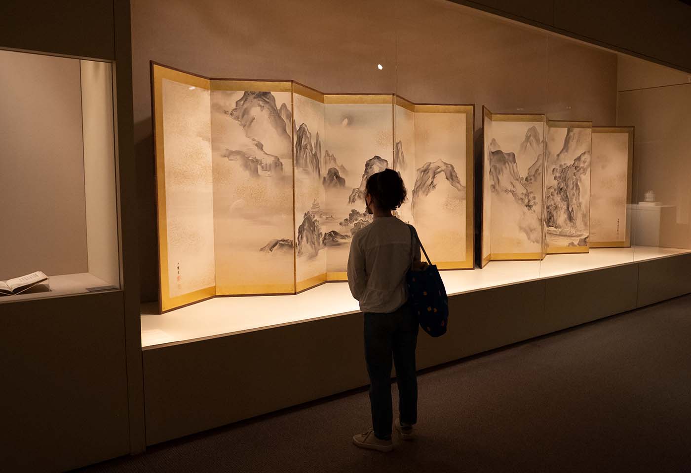 A visitor stands with their back towards the viewer to view Japanese screens featuring a hand painted black ink mountain range.